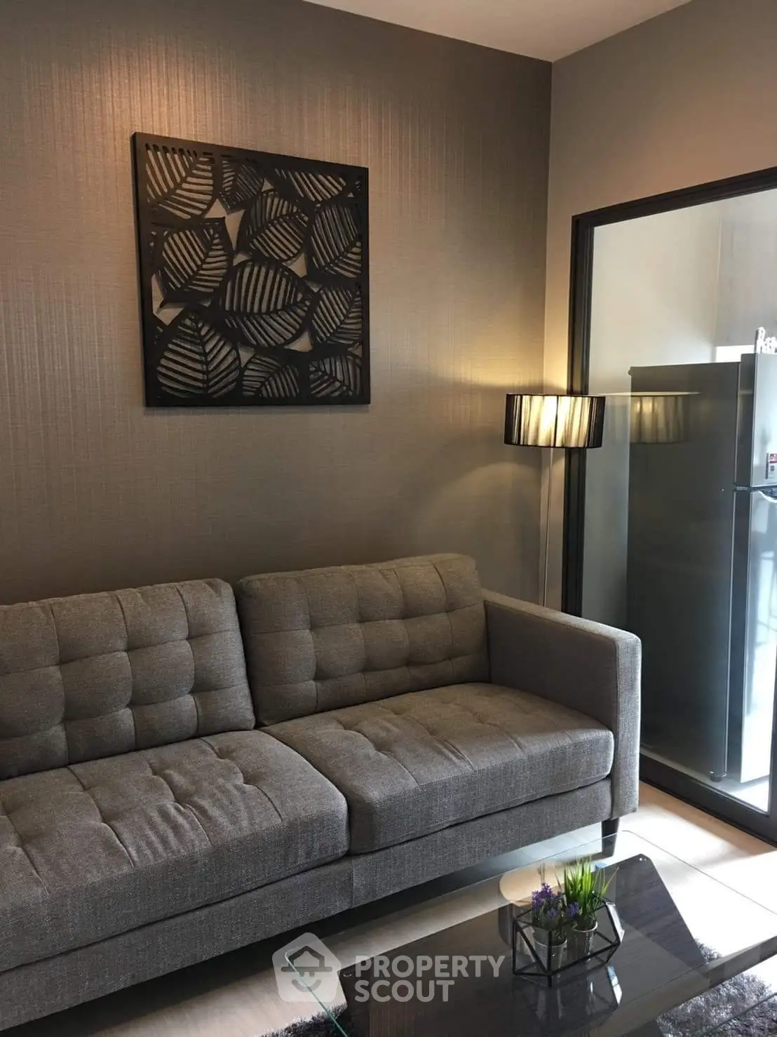 Modern living room with stylish gray sofa and elegant wall art, featuring a sleek glass door leading to a balcony.
