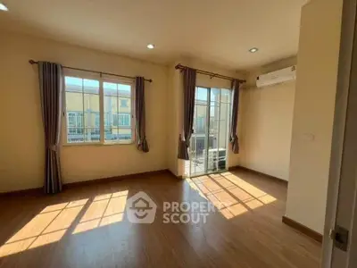 Spacious sunlit room with wooden flooring and large windows in modern apartment.