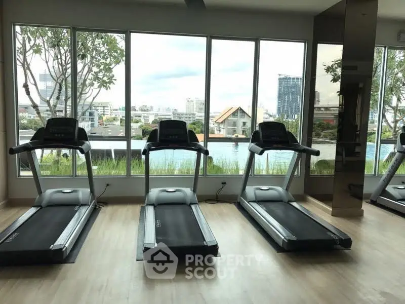 Modern gym with treadmills and scenic city view through large windows.