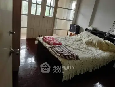 Cozy bedroom with natural light and wooden flooring, featuring a comfortable bed and balcony access.