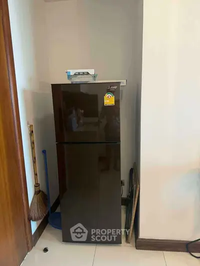 Modern kitchen corner with sleek dark fridge and cleaning tools, perfect for compact spaces.