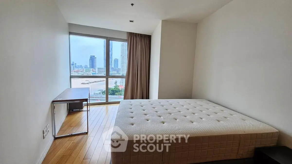 Spacious bedroom with city view and natural light, featuring a large bed and modern desk.