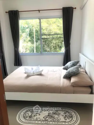 Cozy bedroom with large window and stylish decor, offering a serene view of lush greenery.