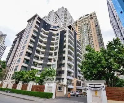 Modern high-rise condominium with lush greenery and elegant entrance in urban setting.