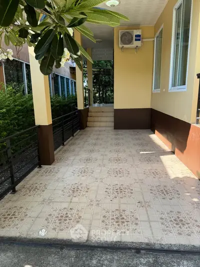 Charming exterior corridor with tiled flooring and lush greenery, perfect for a serene entrance.
