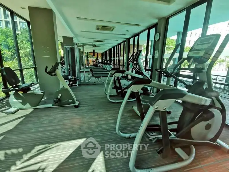 Spacious gym with modern fitness equipment and large windows offering natural light.