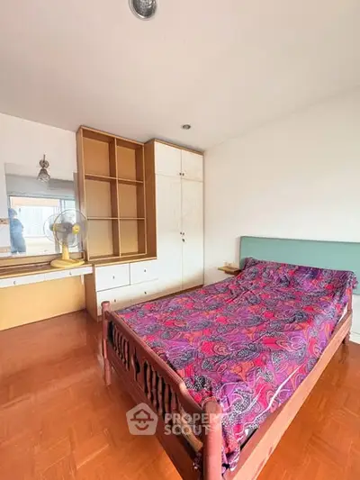Cozy bedroom with wooden flooring and vibrant bedspread, featuring built-in wardrobe and dressing table.