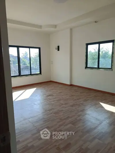 Spacious sunlit room with large windows and wooden flooring, perfect for a cozy living space.