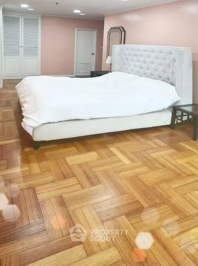Spacious bedroom with elegant parquet flooring and plush headboard, perfect for relaxation.