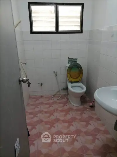 Compact bathroom with pink tile flooring and basic fixtures, featuring a window for natural light.
