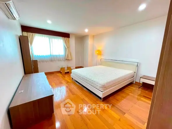 Spacious bedroom with wooden flooring and modern furnishings in a bright apartment.