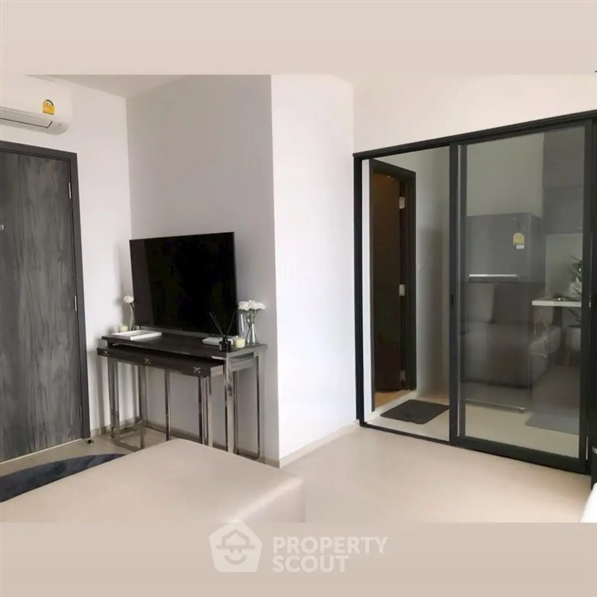 Modern living room with sleek TV setup and glass partition leading to kitchen.