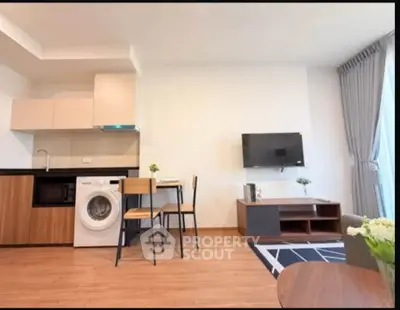 Modern living room with open kitchen and washing machine, featuring stylish decor and natural light.