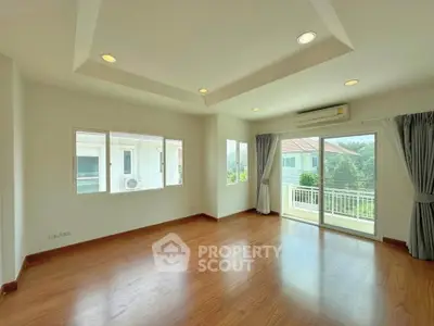 Spacious living room with wooden flooring and large windows offering natural light and garden view.