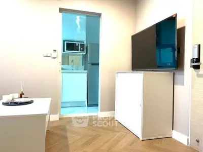 Modern living room with sleek TV setup and view into compact kitchen area.