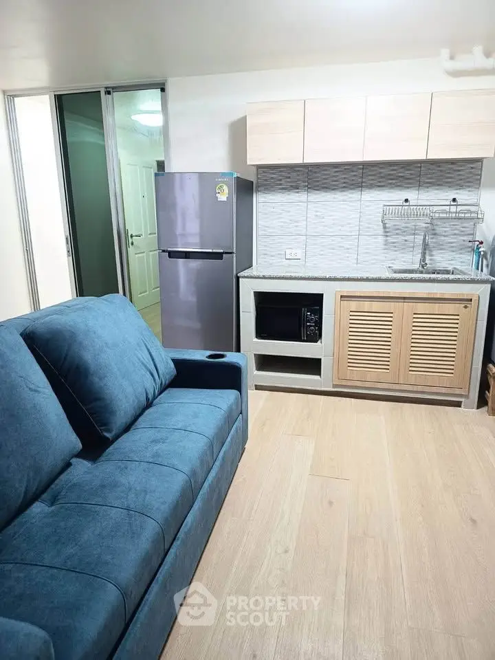 Modern compact kitchen with blue sofa and sleek appliances in cozy apartment