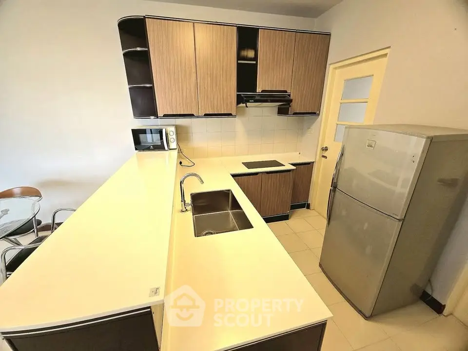 Modern kitchen with sleek cabinets, fridge, and microwave in a stylish apartment.