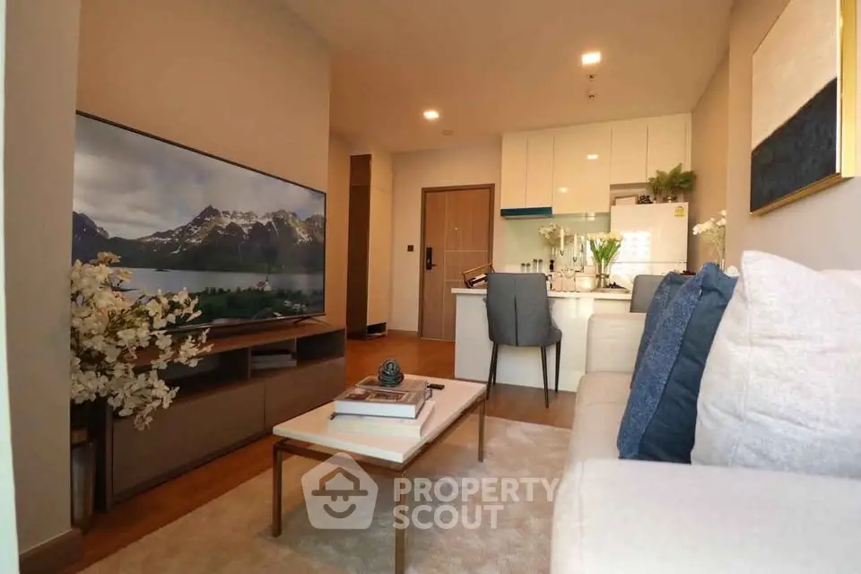 Modern living room with cozy seating and large TV, open to a sleek kitchen area.