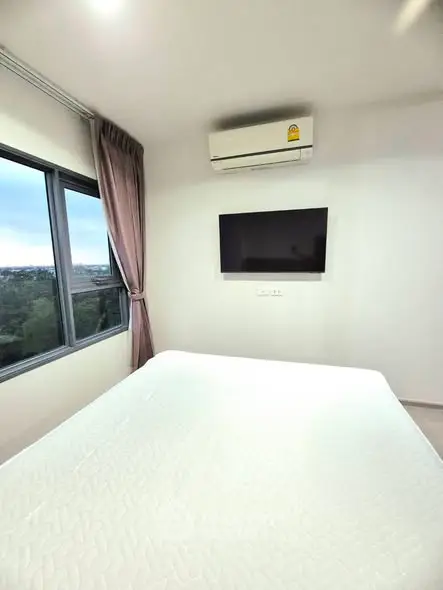 Modern bedroom with large window and wall-mounted TV, featuring a serene view.
