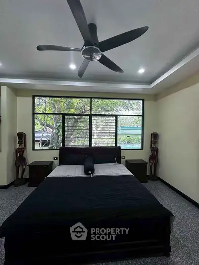 Spacious bedroom with large window and ceiling fan, offering a serene view of greenery.