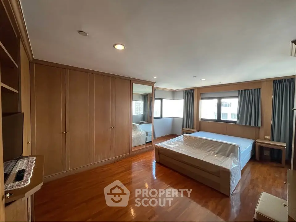 Spacious bedroom with wooden flooring and large windows in a modern apartment.