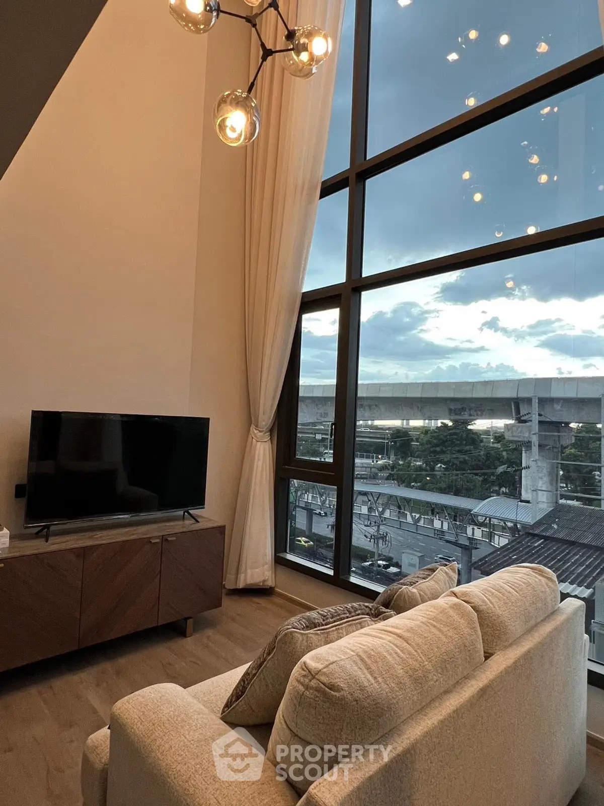 Modern living room with high ceilings and large windows offering stunning city views.