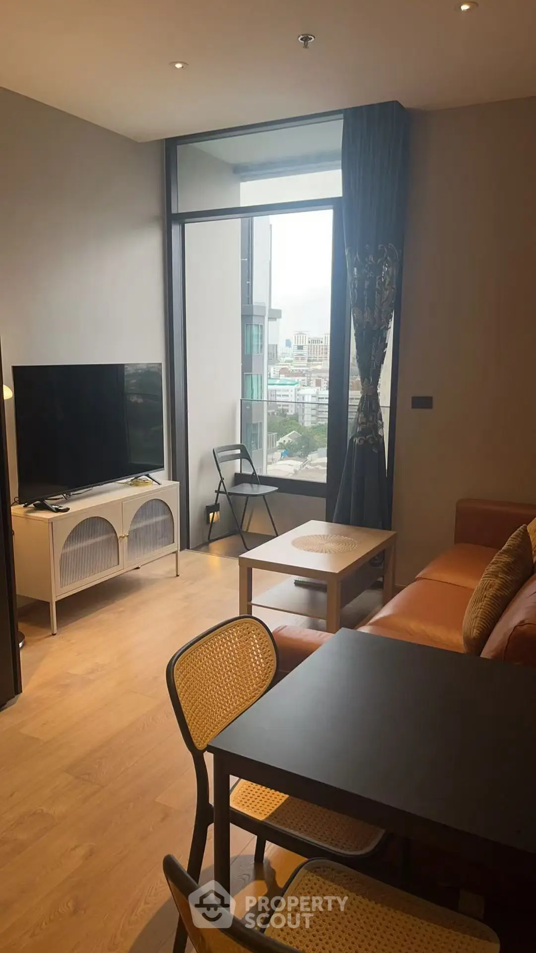Modern living room with large window and city view, featuring stylish furniture and a flat-screen TV.