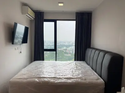 Modern bedroom with city view, featuring a large window, wall-mounted TV, and air conditioning.