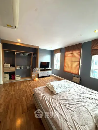 Spacious bedroom with wooden flooring, large windows, and built-in closet in modern apartment.