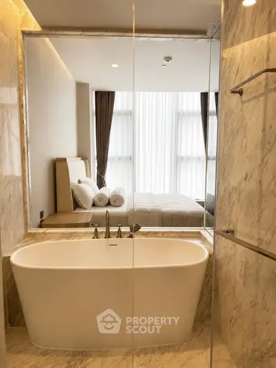 Luxurious bathroom with marble finishes and a freestanding bathtub overlooking a modern bedroom.