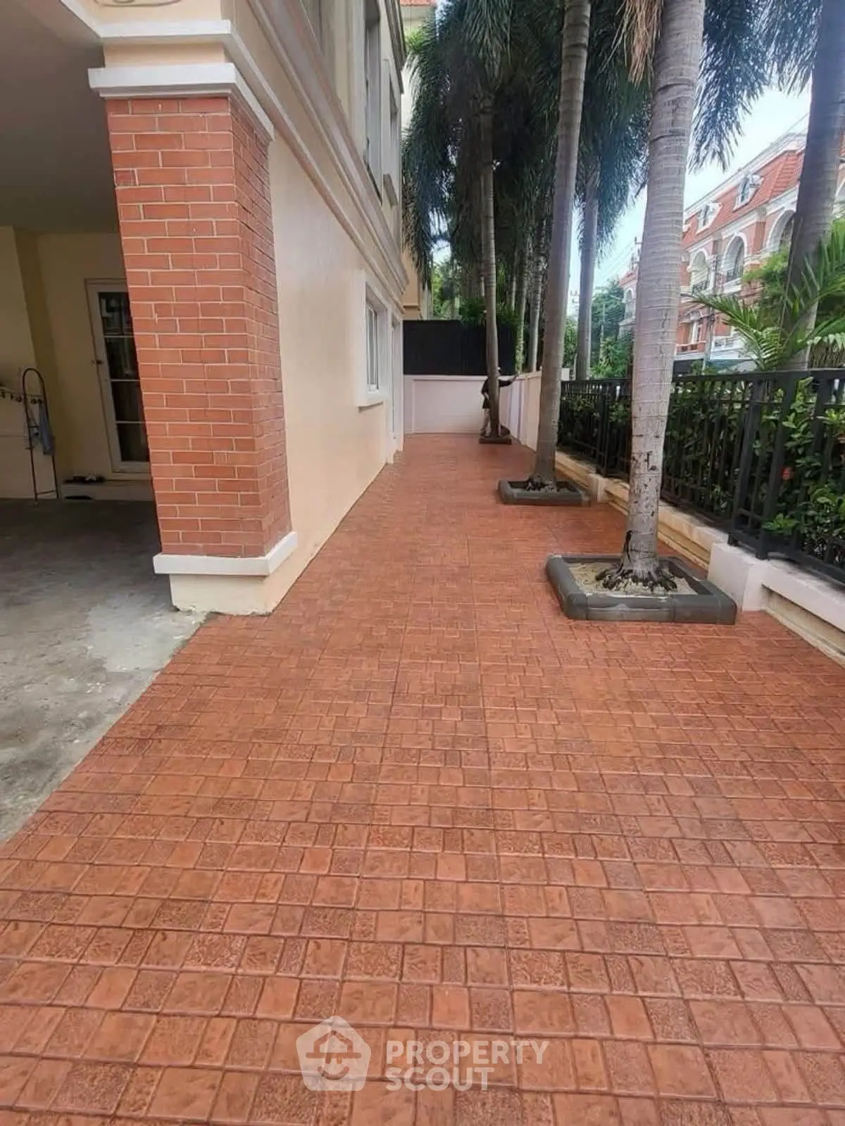 Charming exterior walkway with brick tiles and lush palm trees, perfect for a serene residential setting.