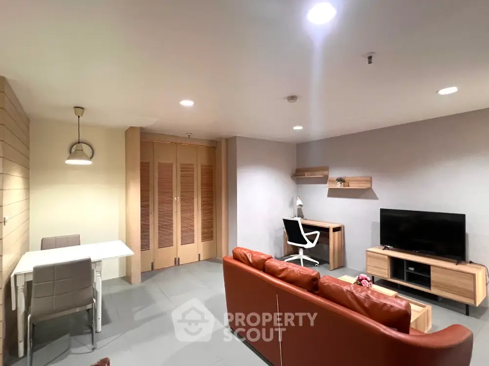 Modern living room with leather sofa, TV, and study desk in open layout apartment.