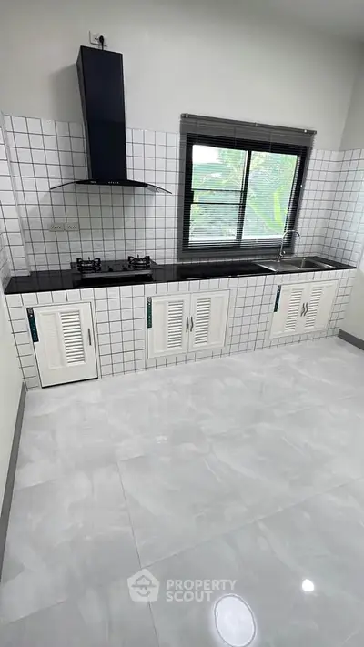 Modern kitchen with sleek black countertop and gas stove in a bright, tiled space.
