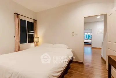 Cozy bedroom with wooden flooring and soft lighting, featuring a comfortable bed and window view.