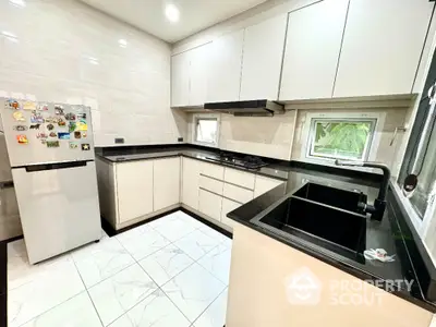 Modern kitchen with sleek cabinetry and black countertops, featuring a gas stove and refrigerator.