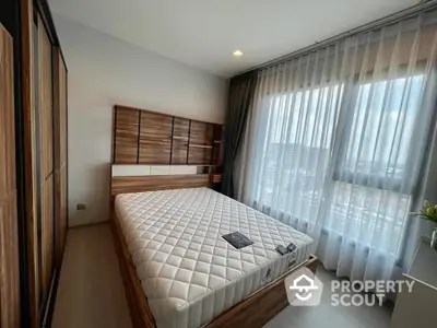 Spacious bedroom with large bed and modern wooden headboard, floor-to-ceiling sheer curtains, and warm ambient lighting.