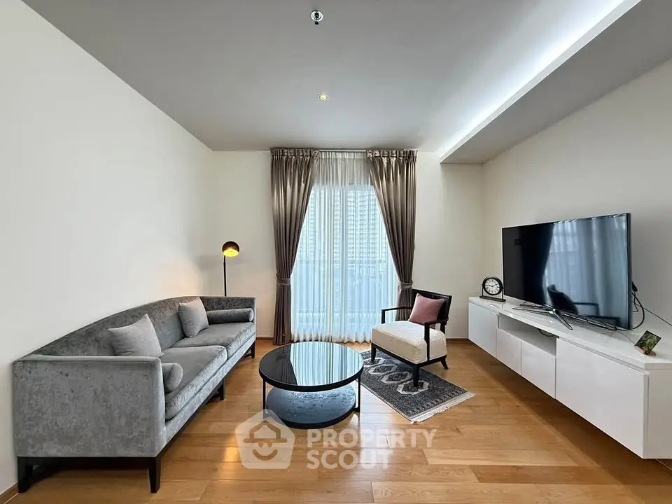 Modern living room with sleek furniture and large TV, featuring elegant curtains and wooden flooring.