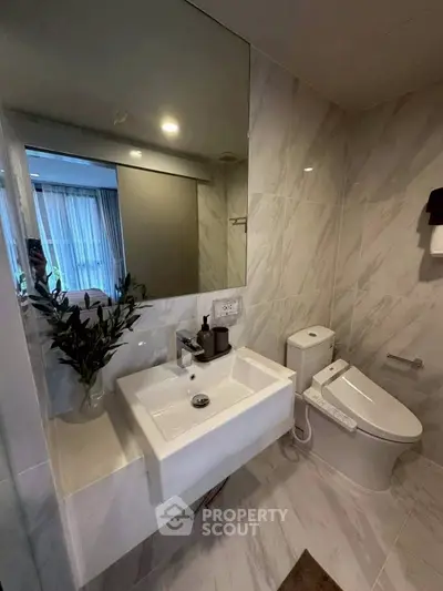 Modern bathroom with sleek fixtures and elegant marble tiles, featuring a stylish sink and toilet.