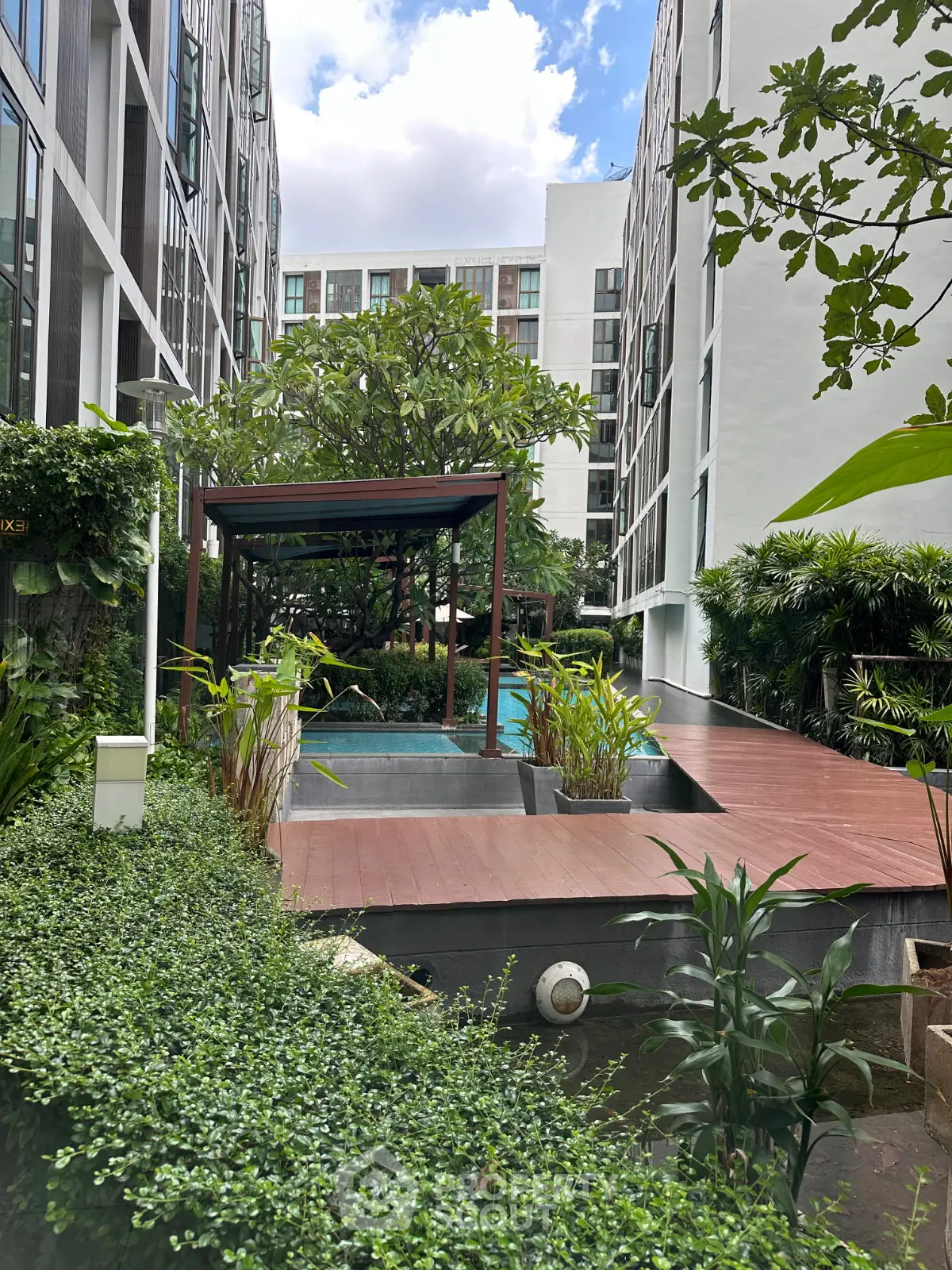 Modern apartment complex with lush greenery and poolside relaxation area.