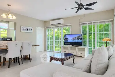 Spacious living room with modern decor and large windows offering lush green views.