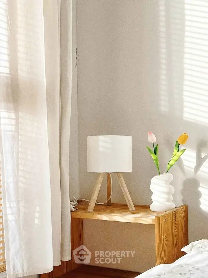 Cozy bedroom corner with wooden nightstand, modern lamp, and decorative vase with tulips.