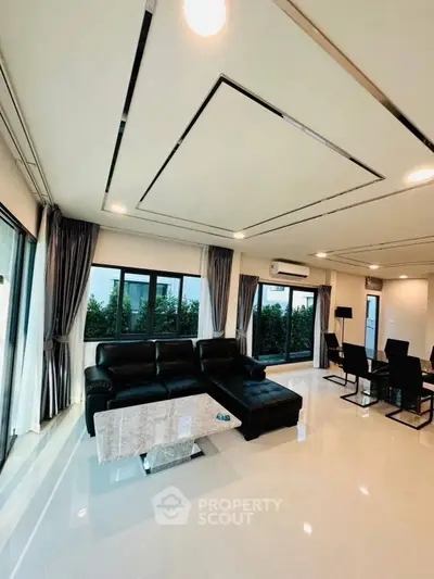 Spacious modern living room with sleek black furniture and large windows offering lush garden views.
