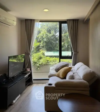 Cozy living room with large window and lush garden view, featuring a comfortable sofa and modern TV setup.