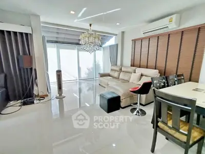 Spacious living room with modern decor and natural light, featuring a chandelier and comfortable seating.