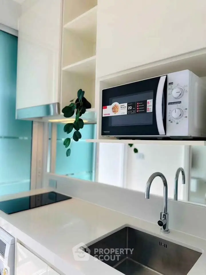 Modern kitchen with sleek white countertops, built-in microwave, and stainless steel sink.