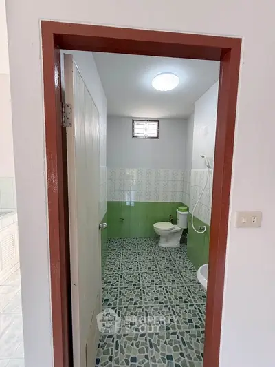 Spacious bathroom with green and white tiles, featuring a modern toilet and shower area.