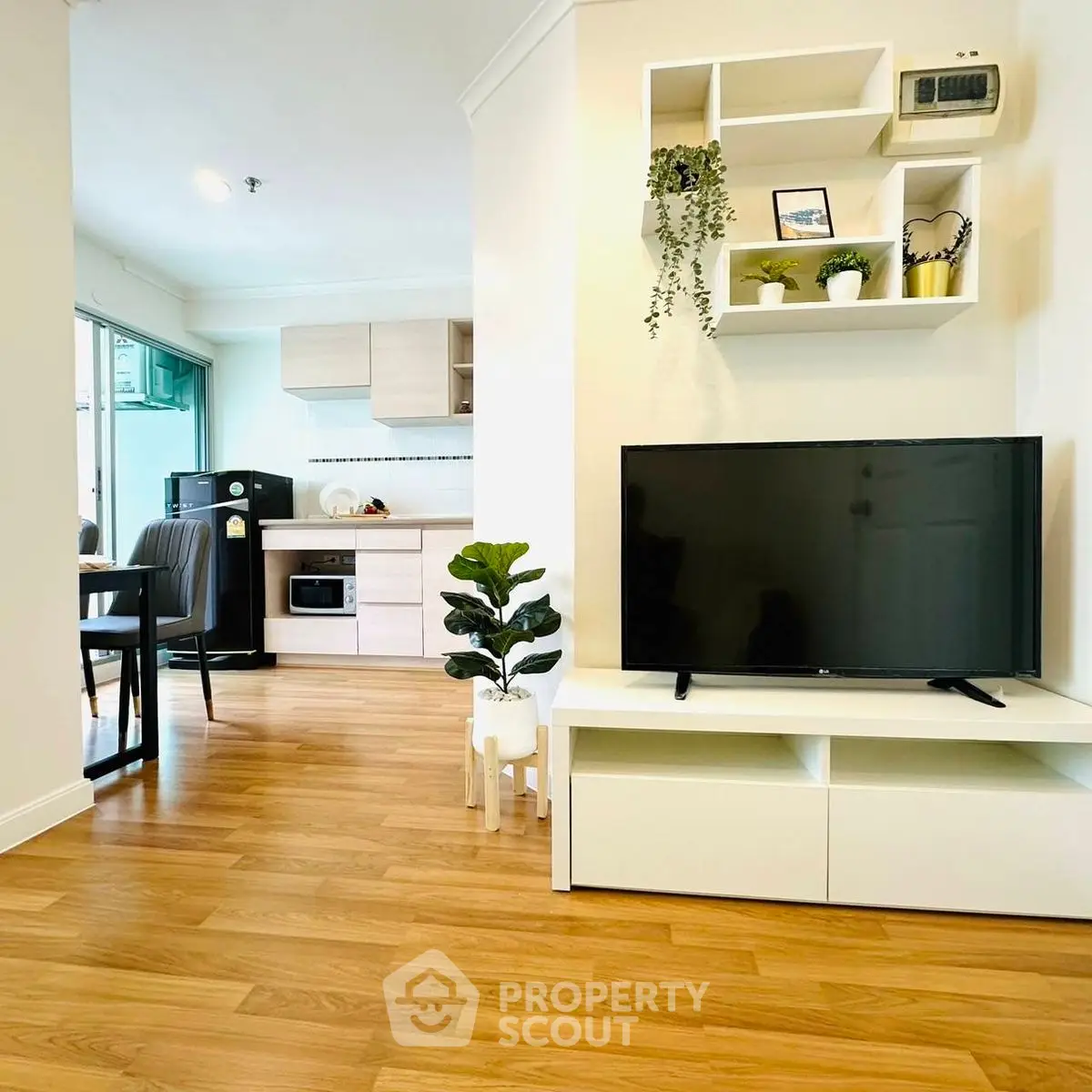 Modern living room with TV and open kitchen, wooden flooring, and stylish decor.
