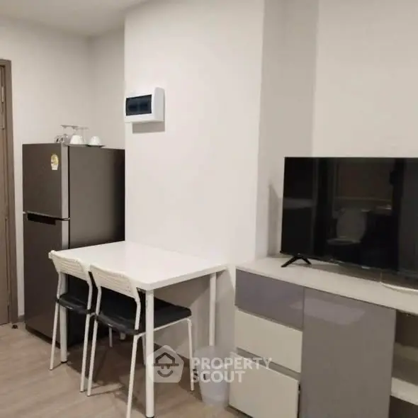 Modern apartment interior with dining area and TV setup, featuring sleek furniture and neutral tones.