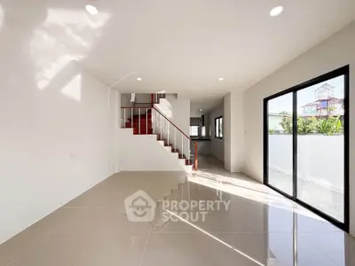 Spacious modern living room with sleek staircase and large windows for natural light.