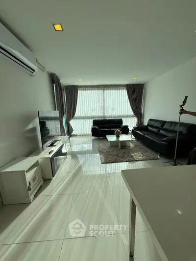 Spacious living room with modern black leather sofas and large windows.